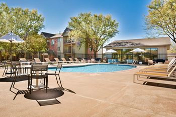 Outdoor pool with spacious deck lined with lounge chairs and tables.